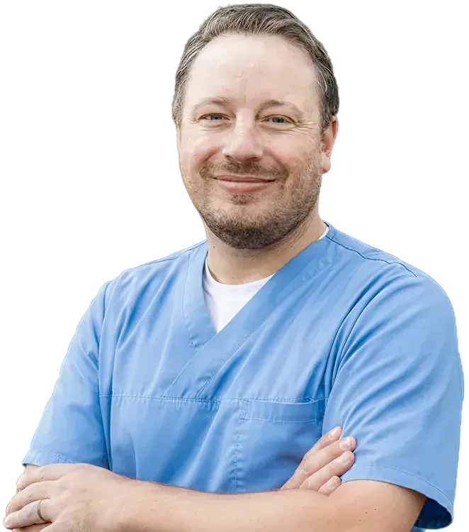 Smiling Dr Jeramiah Paylor wearing blue scrubs with arms crossed.