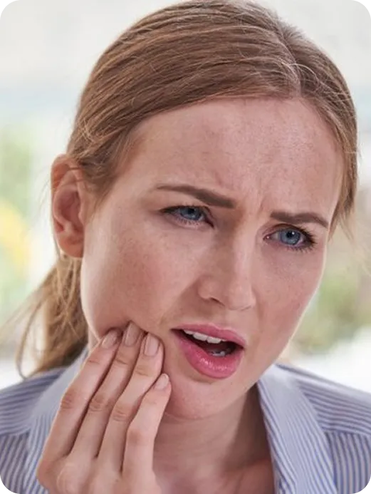 Woman with blonde hair holding her cheek and showing a pained expression, suggesting toothache or jaw pain.