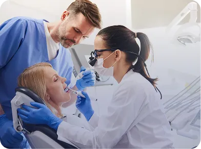 Dentist and dental assistant examining and treating a woman patient seated in a dental chair.