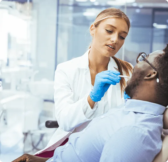 Healthcare professional wearing blue gloves examining a patient's mouth with a tongue depressor in a clinical setting.