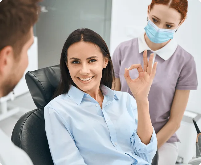 Smiling man sitting in a dental chair giving a thumbs-up in a bright dental office.