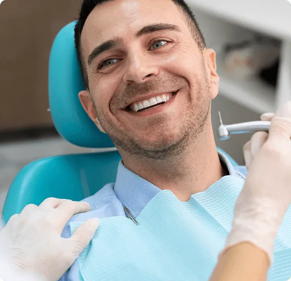 Modern dental examination room with a black and white dental chair, dental equipment, a large mirror on gray wall, and a mounted TV screen.