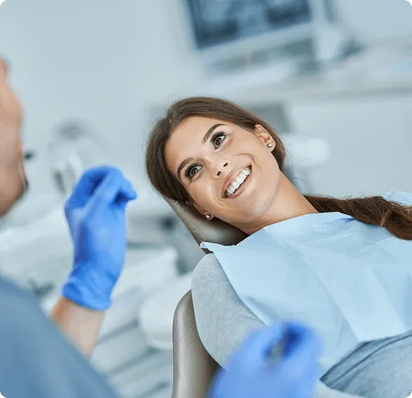 Smiling woman reclined in a dental chair, interacting with a dentist wearing blue gloves.