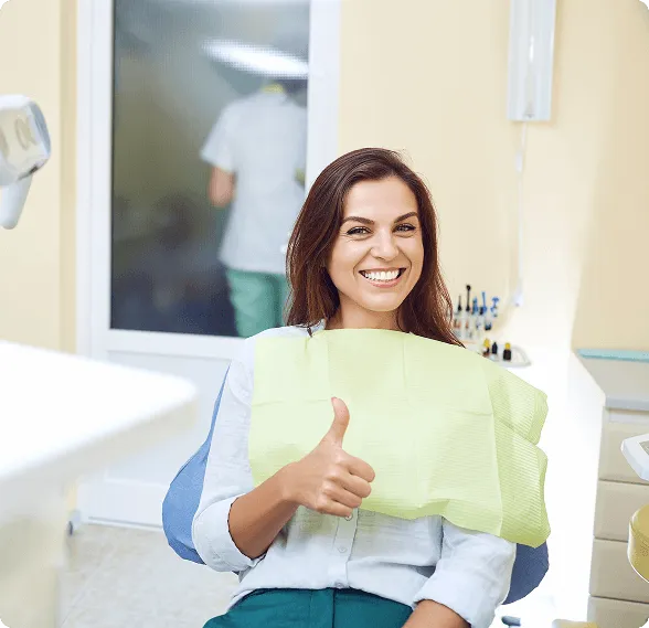 Smiling woman sitting in a dental chair giving a thumbs-up with a dental bib.