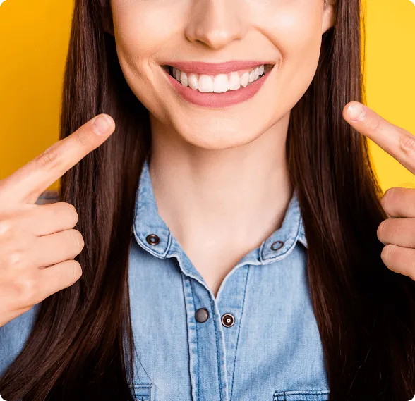 Woman smiling and pointing at her bright white teeth against a yellow background.