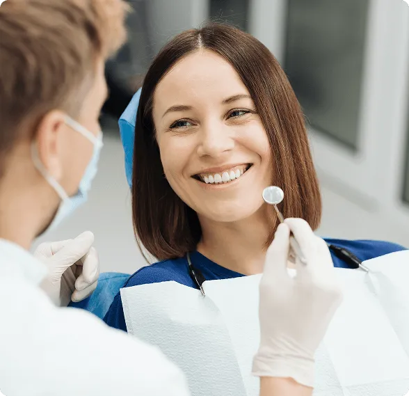 Smiling woman in a dental chair looking at a masked dentist holding a dental mirror.