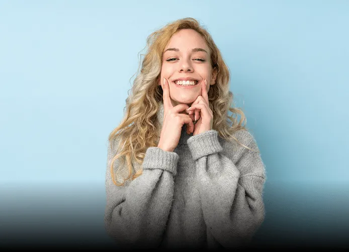 Young woman with long brown hair winking and smiling while taking a selfie outdoors, holding up a peace sign.