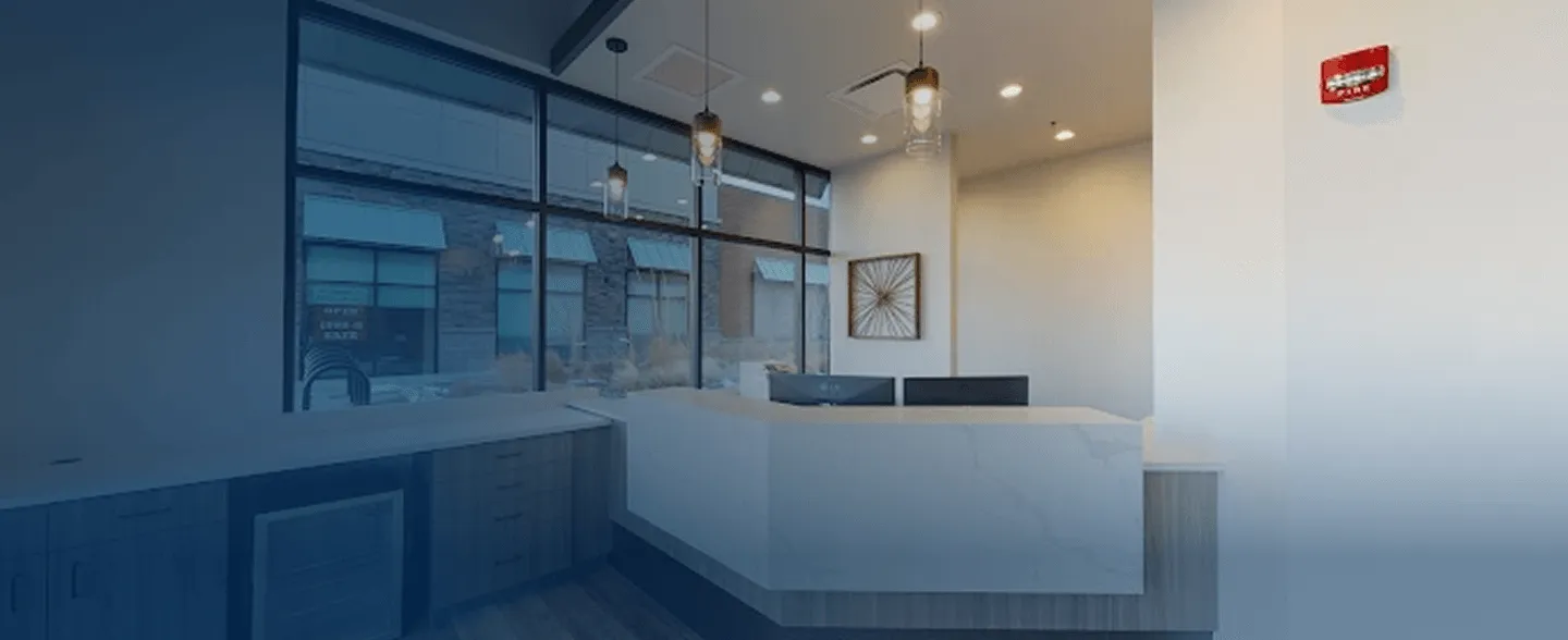 Modern reception desk with marble countertop, two computer monitors, pendant lights, and large windows showing exterior building.