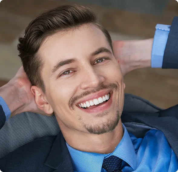 Smiling man sitting in a dental chair giving a thumbs-up in a bright dental office.