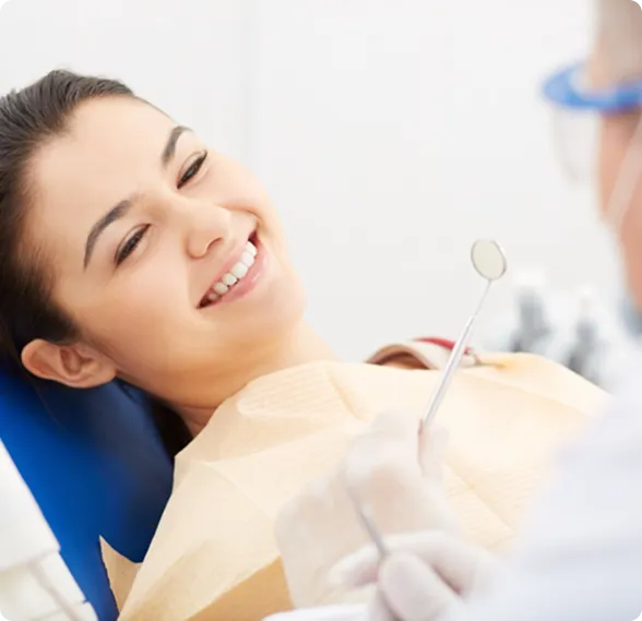 Smiling woman reclined in a dental chair, interacting with a dentist wearing blue gloves.