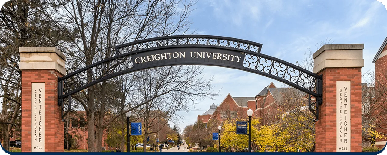 Aerial view of a university campus with red-roofed buildings, a large stadium, surrounded by trees and mountains in the background.