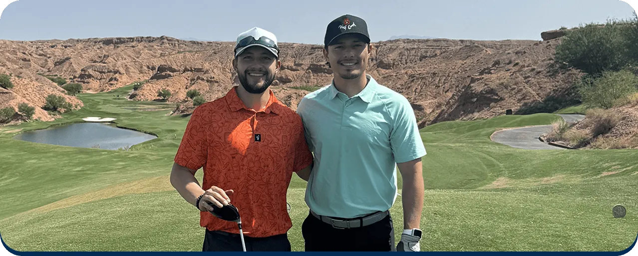 Smiling family of five sitting outdoors on rocky terrain with dry grass in the background.