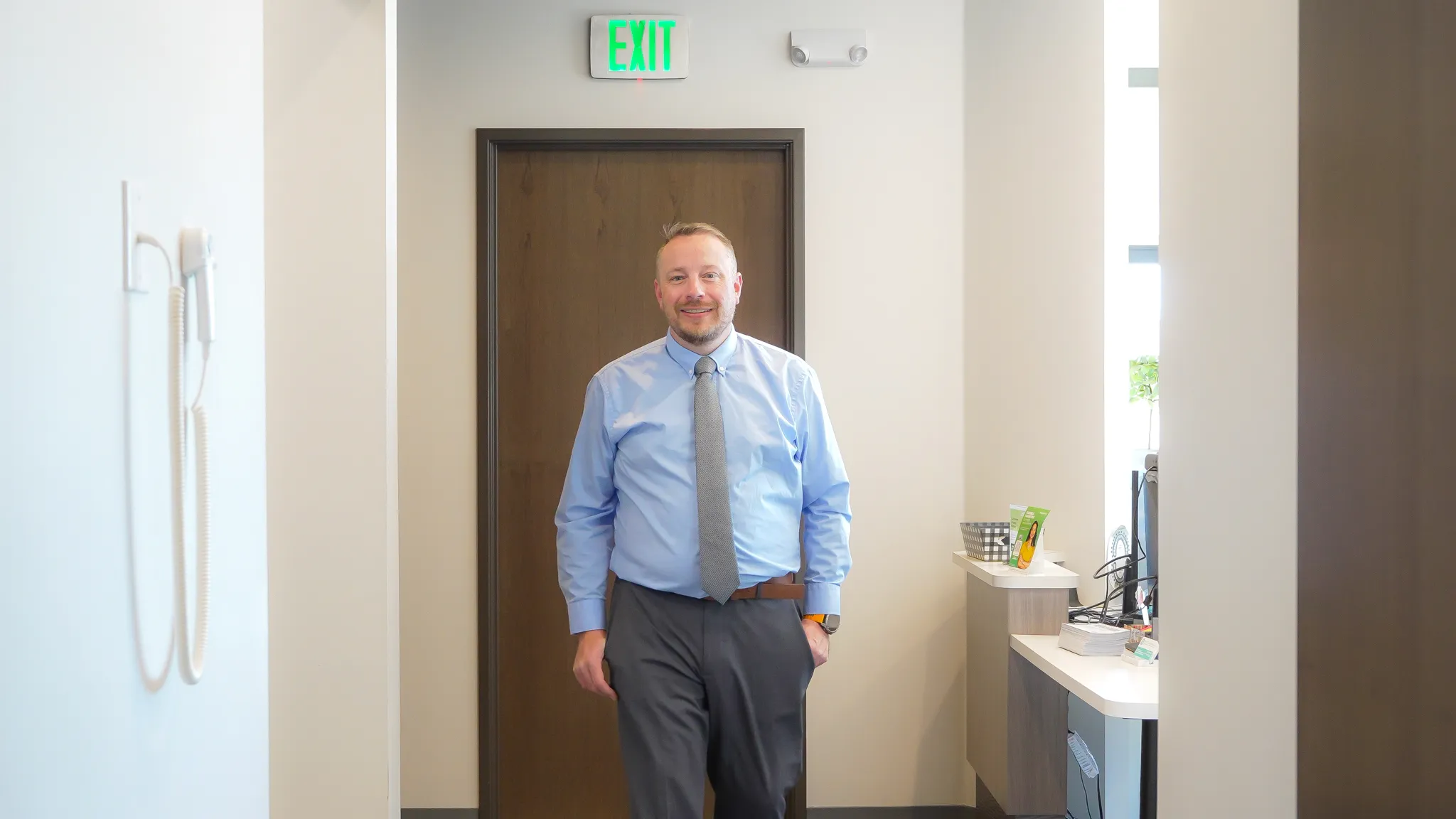 Modern dental examination room with a black and white dental chair, dental equipment, a large mirror on gray wall, and a mounted TV screen.