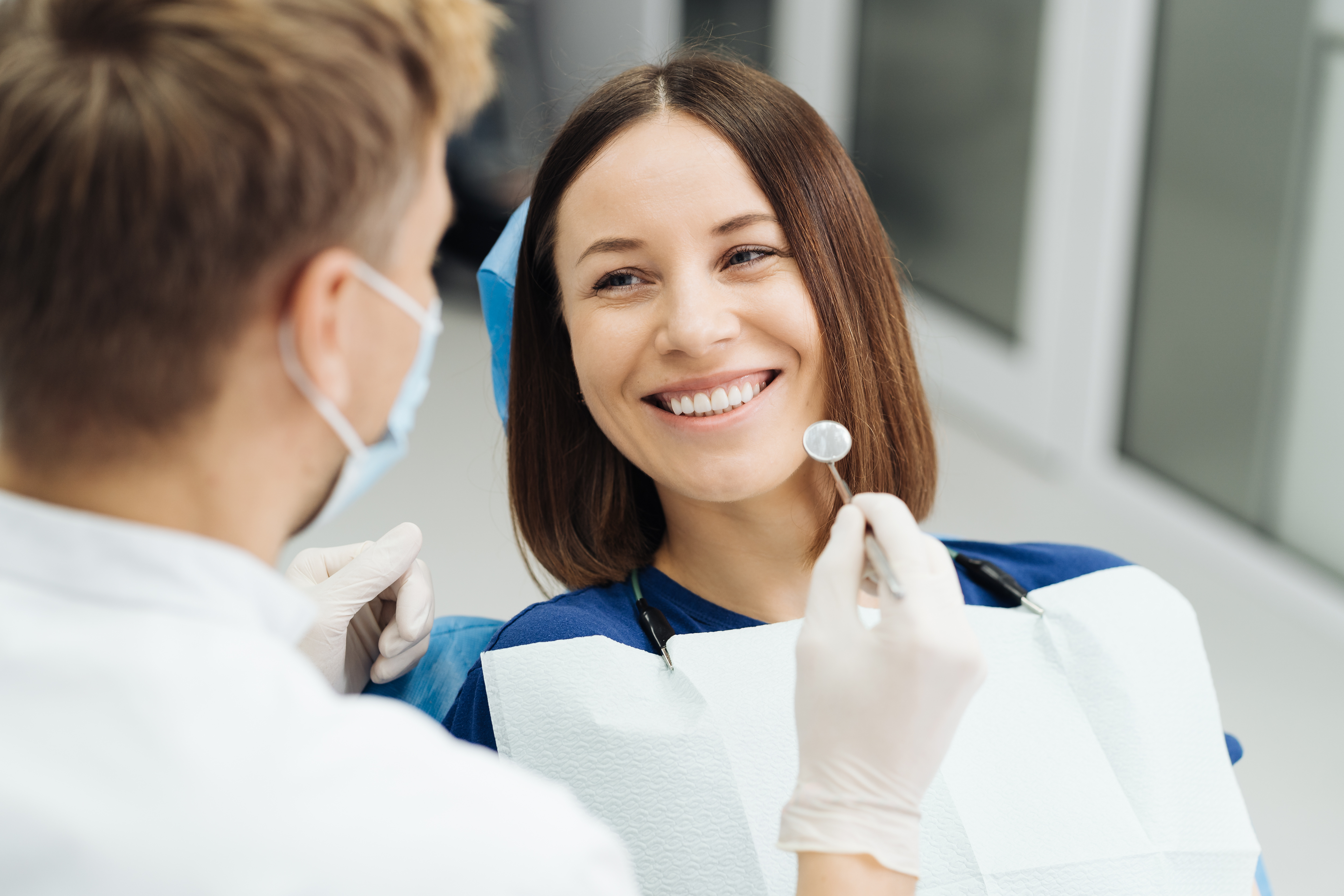 Smiling woman reclined in a dental chair, interacting with a dentist wearing blue gloves.