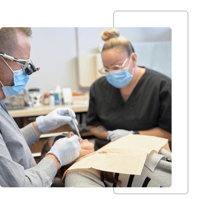 Dentist holding a dental shade guide near a smiling woman's teeth to match tooth color.