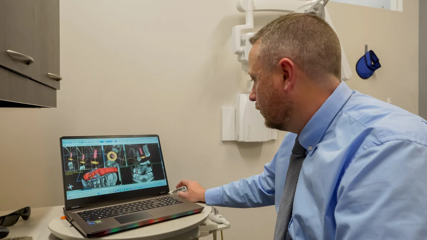 Smiling man sitting in a dental chair giving a thumbs-up in a bright dental office.
