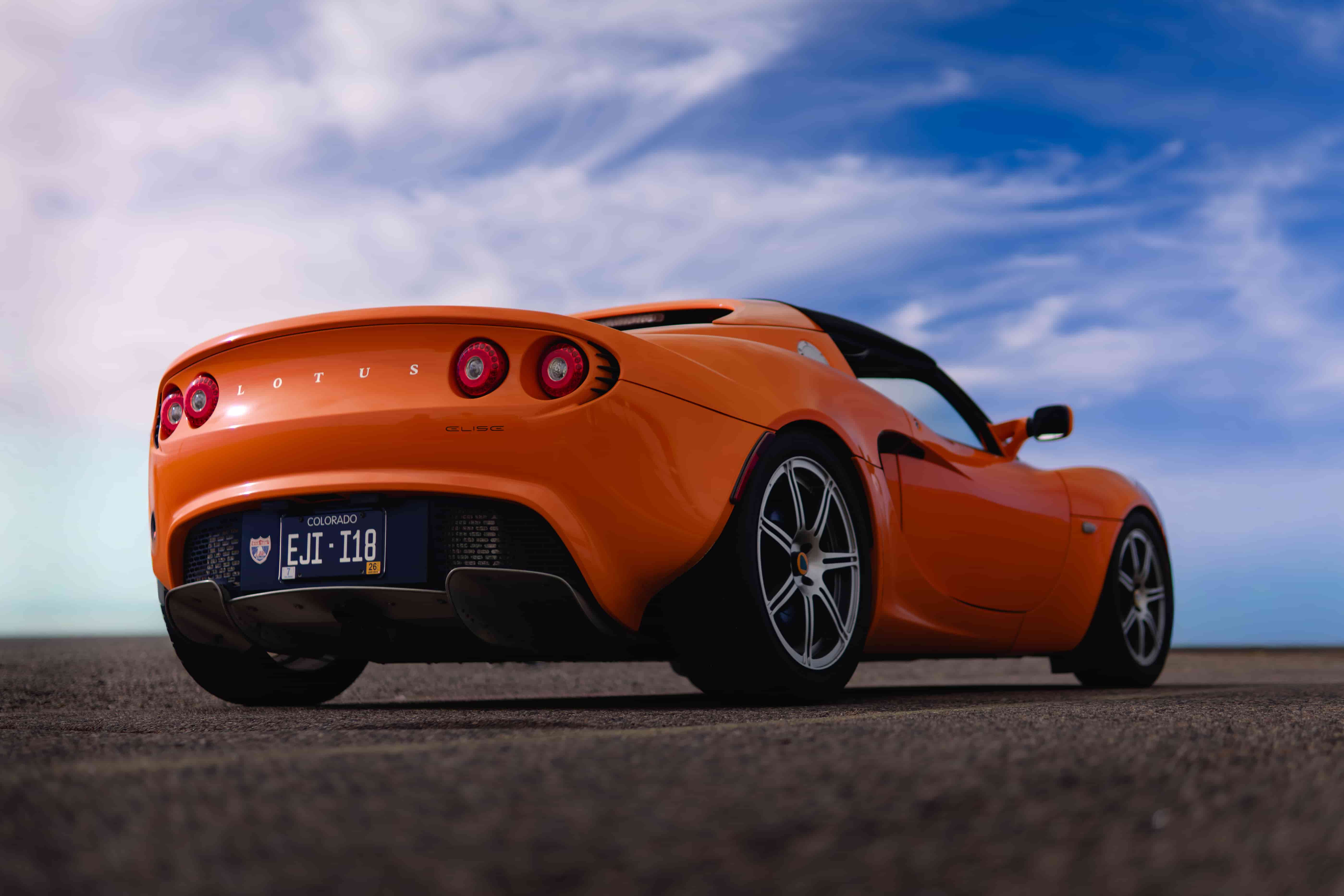 Orange Lotus Elise sports car used for racing with a cloudy blue sky