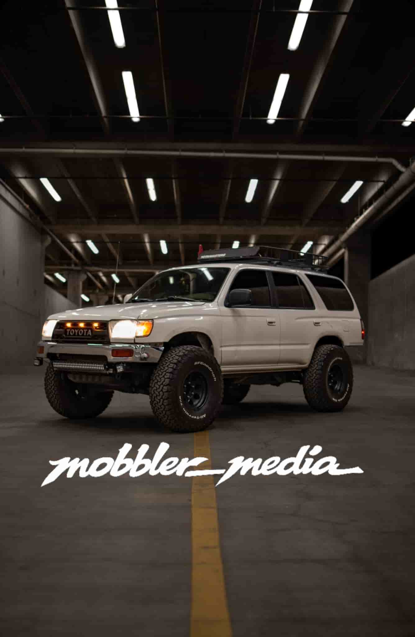 White Toyota SUV with off-road tires under warehouse ceiling lights.