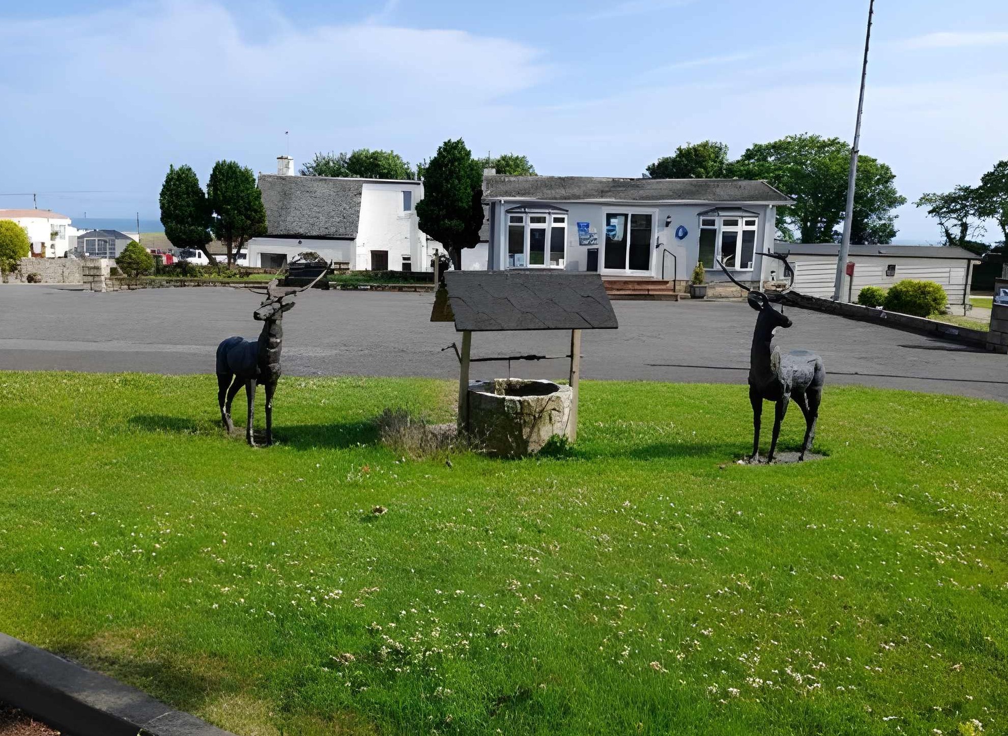 Two deer statues by old well in front of coastal buildings