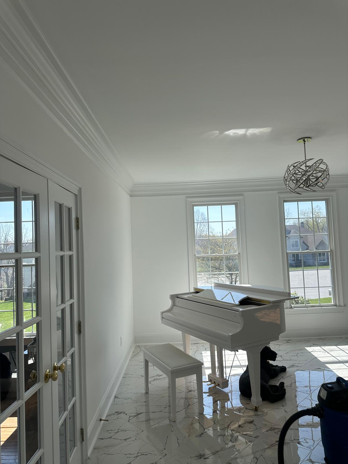 Bright room with a white grand piano, matching bench, three large windows, and a black dog lying on glossy marble floor tiles.