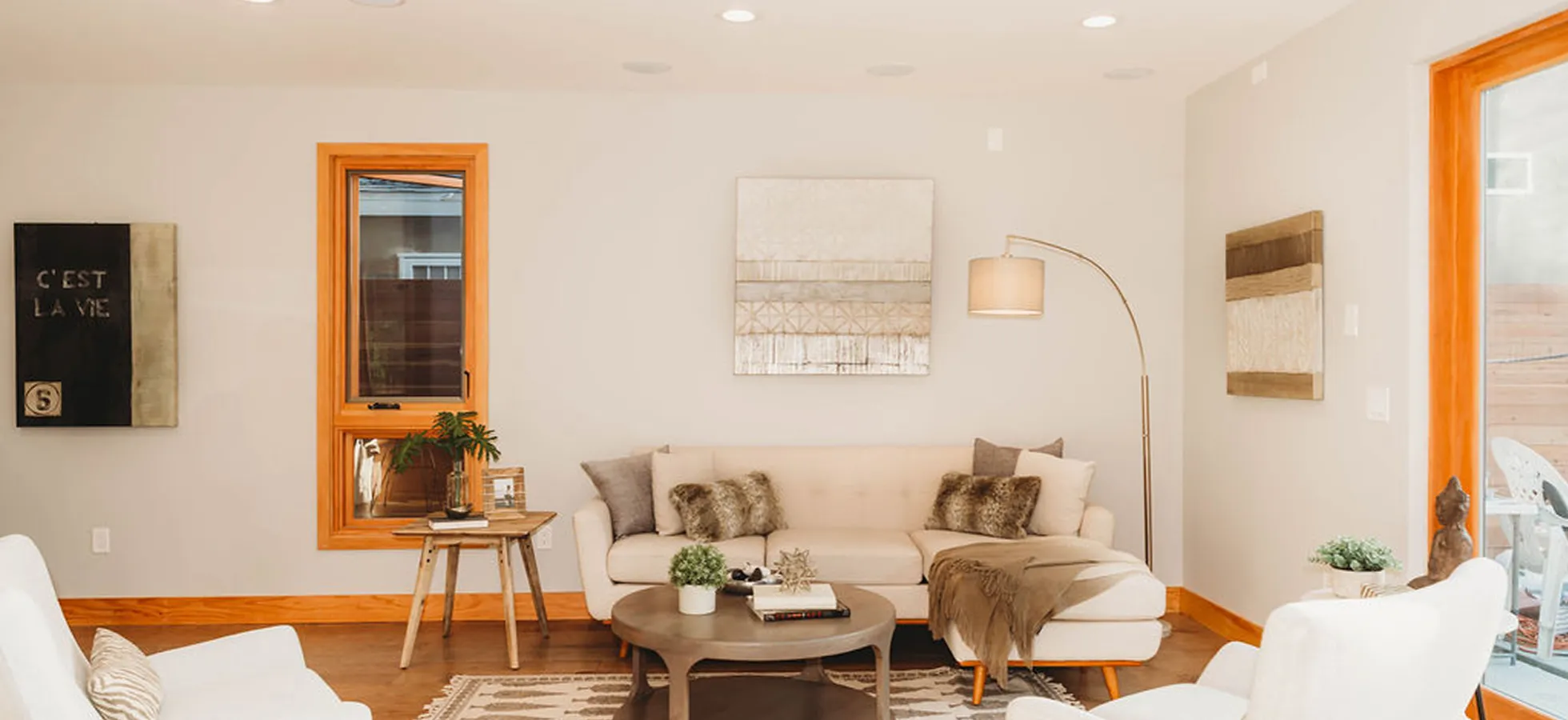 Cozy living room with a beige sectional sofa, white armchairs, wooden coffee table, and warm neutral decor.