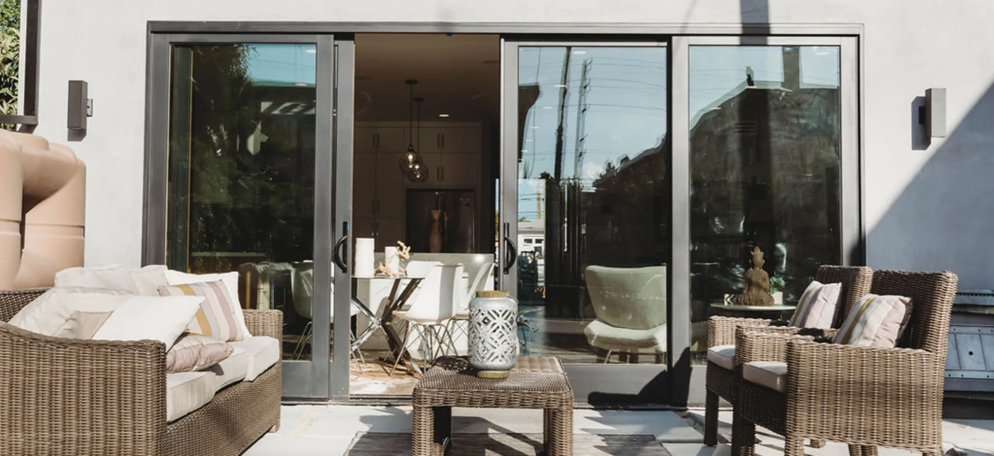 Outdoor patio with wicker seating including a sofa and two chairs with cushions, a matching wicker coffee table, and sliding glass doors leading to an indoor dining area.
