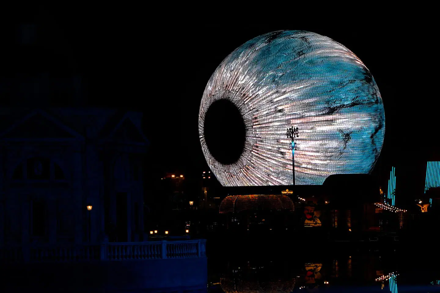 SELA Sphere at night with a circular opening at center, displaying ocean texture visuals across the spherical LED surface