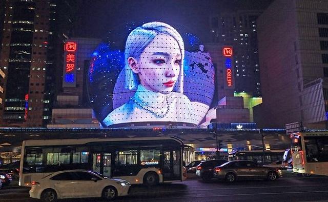 Street-level view of the Naked Eye 3D Dome at Metro City Shanghai displaying a woman's face in 3D on the transparent spherical LED facade at night