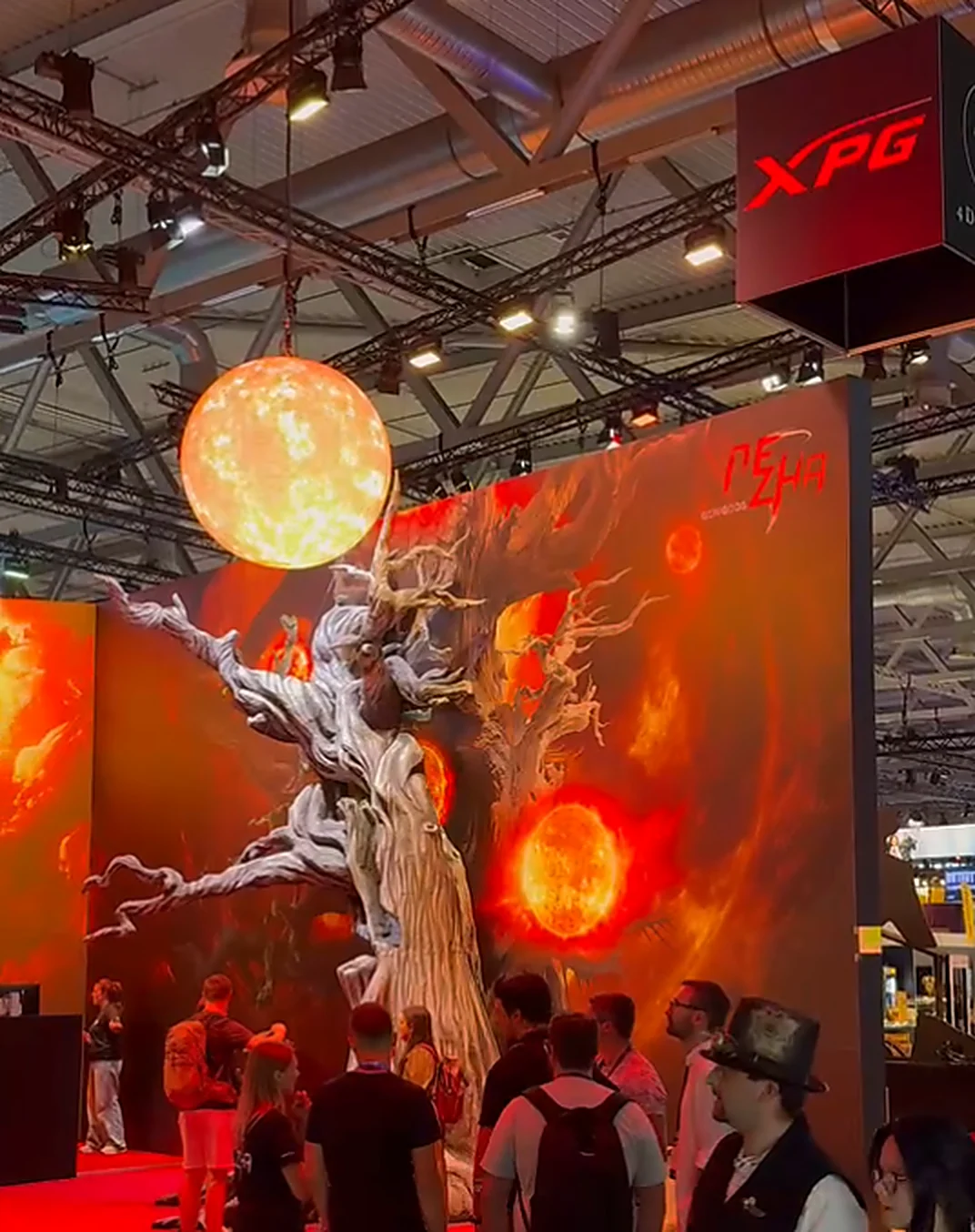 Hanging sphere LED displaying a glowing sun planet above a sculpted tree at the XPG exhibition booth
