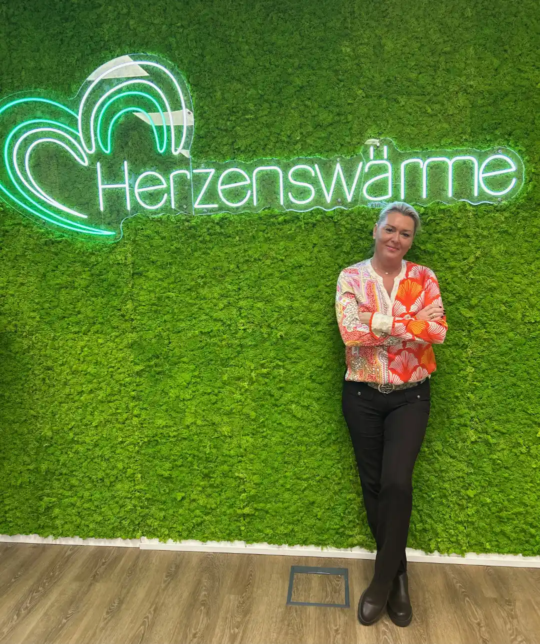 Geschäftsführerin Eva Reimann vor Mooswand mit Logo und Schriftzug "Herzenswärme"