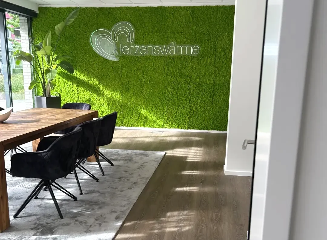 Besprechungsraum mit grüner Mooswand mit Logo und Schriftzug "Herzenswärme"