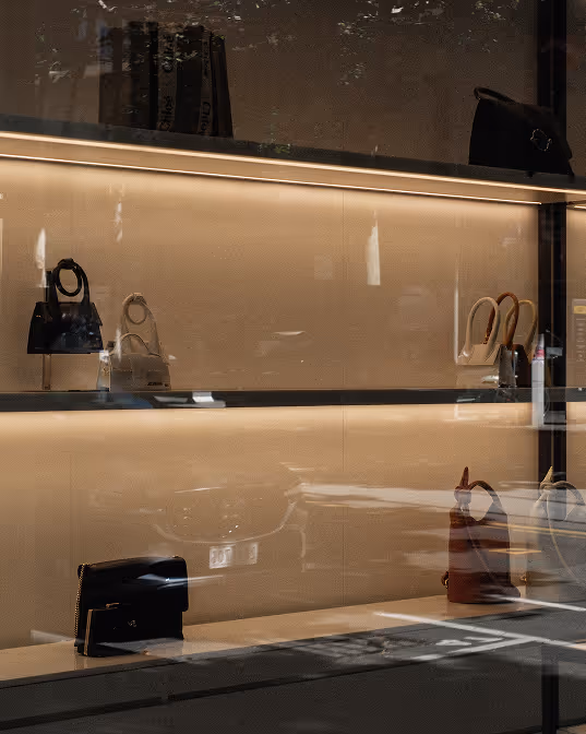 Elegant display of various handbags on illuminated shelves in a luxury boutique window.