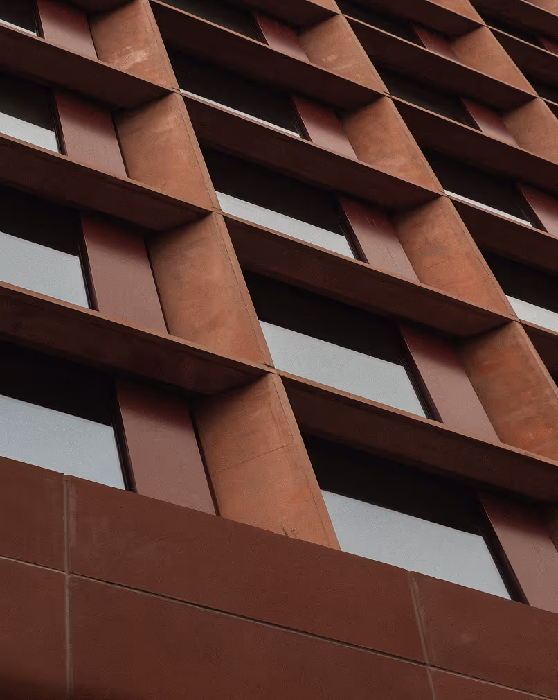 Close-up view of a building facade with a geometric pattern of brown protruding rectangular frames around windows.