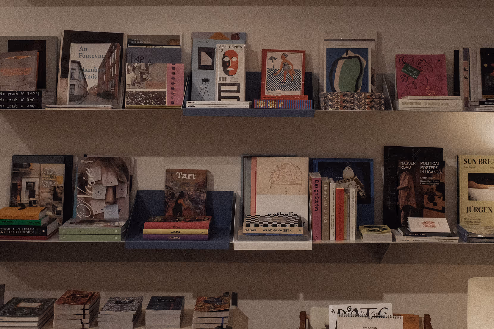 Shelves filled with assorted books and magazines arranged both vertically and horizontally against a beige wall.