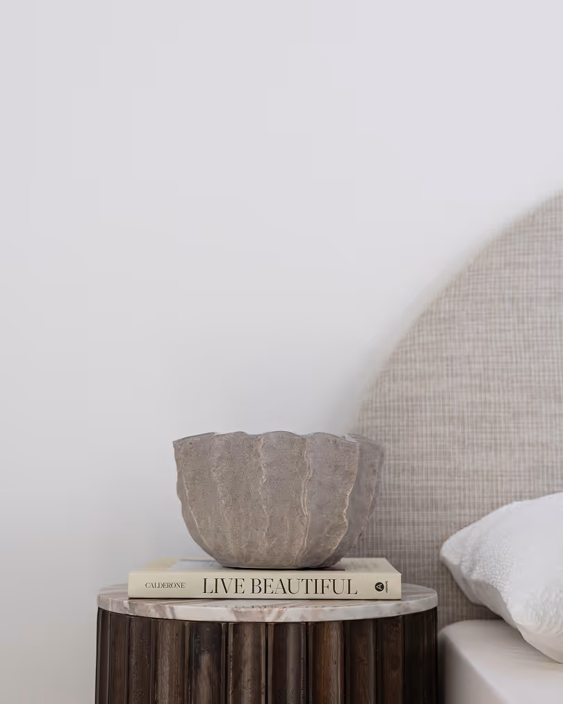 Minimalist bedside table with a textured gray bowl on top of a book titled 'Live Beautiful'.