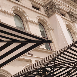 Black and white striped awnings in front of a beige historic building with arched windows.