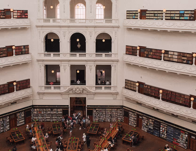 Interior view of a grand library with multiple balcony levels filled with books and people studying at desks below.