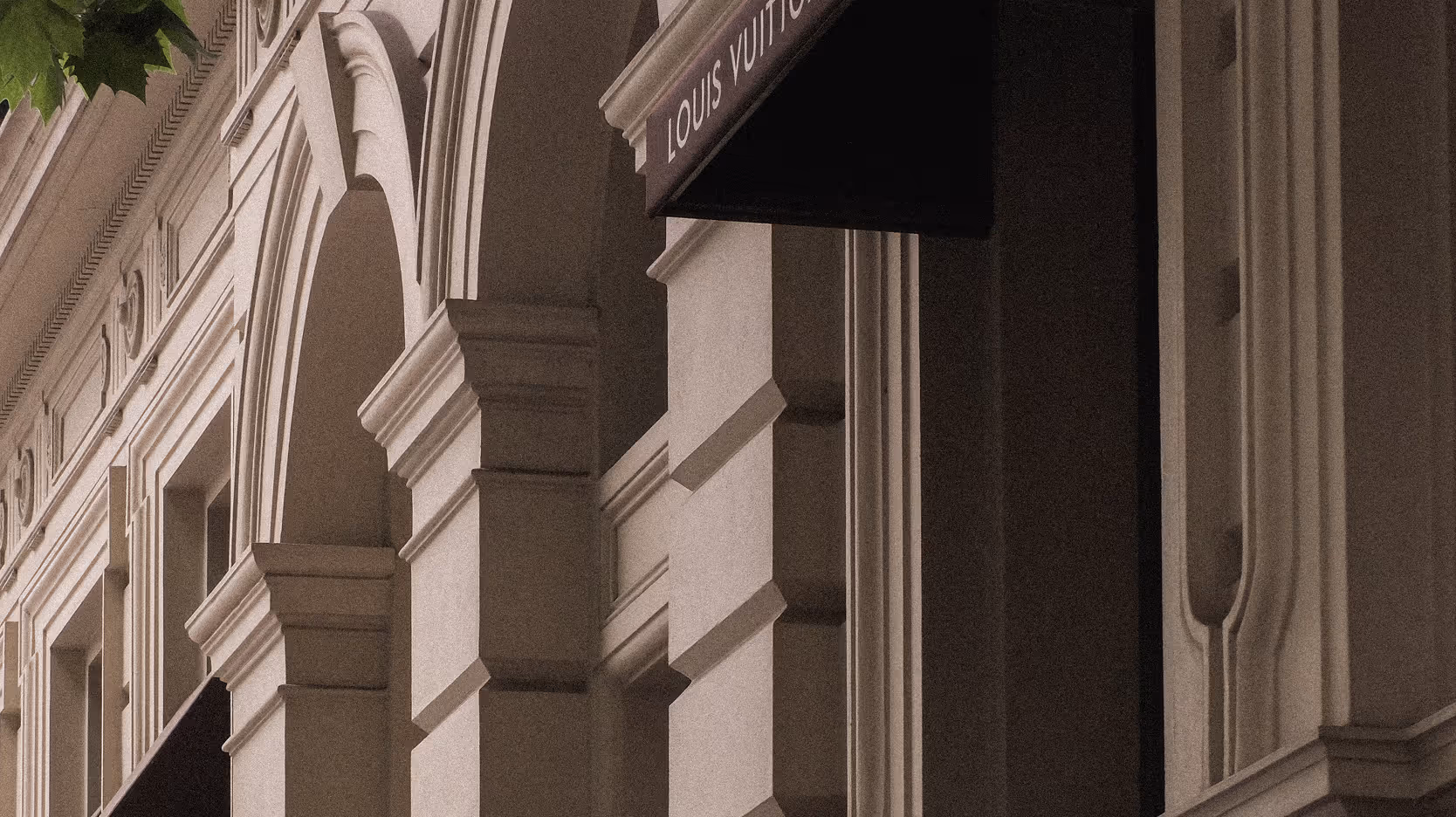 Close-up of elegant architectural columns and arches on a building facade with a black Louis Vuitton store sign.
