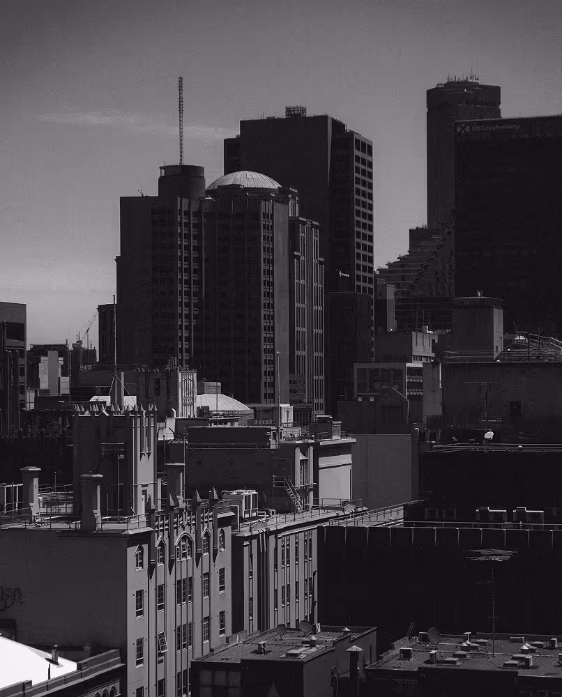 Black and white photograph of a dense urban cityscape with a mix of historic and modern high-rise buildings under a clear sky.