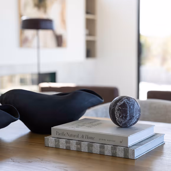 Black stone sphere placed on top of two stacked books on a wooden table with a modern black decorative piece in the background.