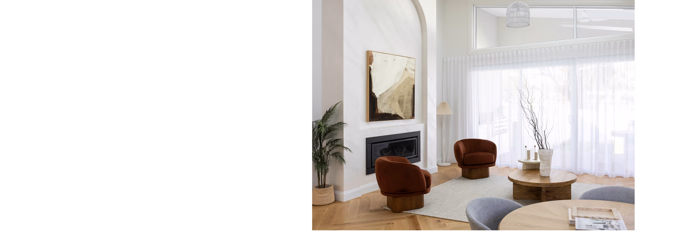 Bright modern living room with two brown swivel chairs, round wooden coffee table, abstract painting above fireplace, and large sheer curtains.