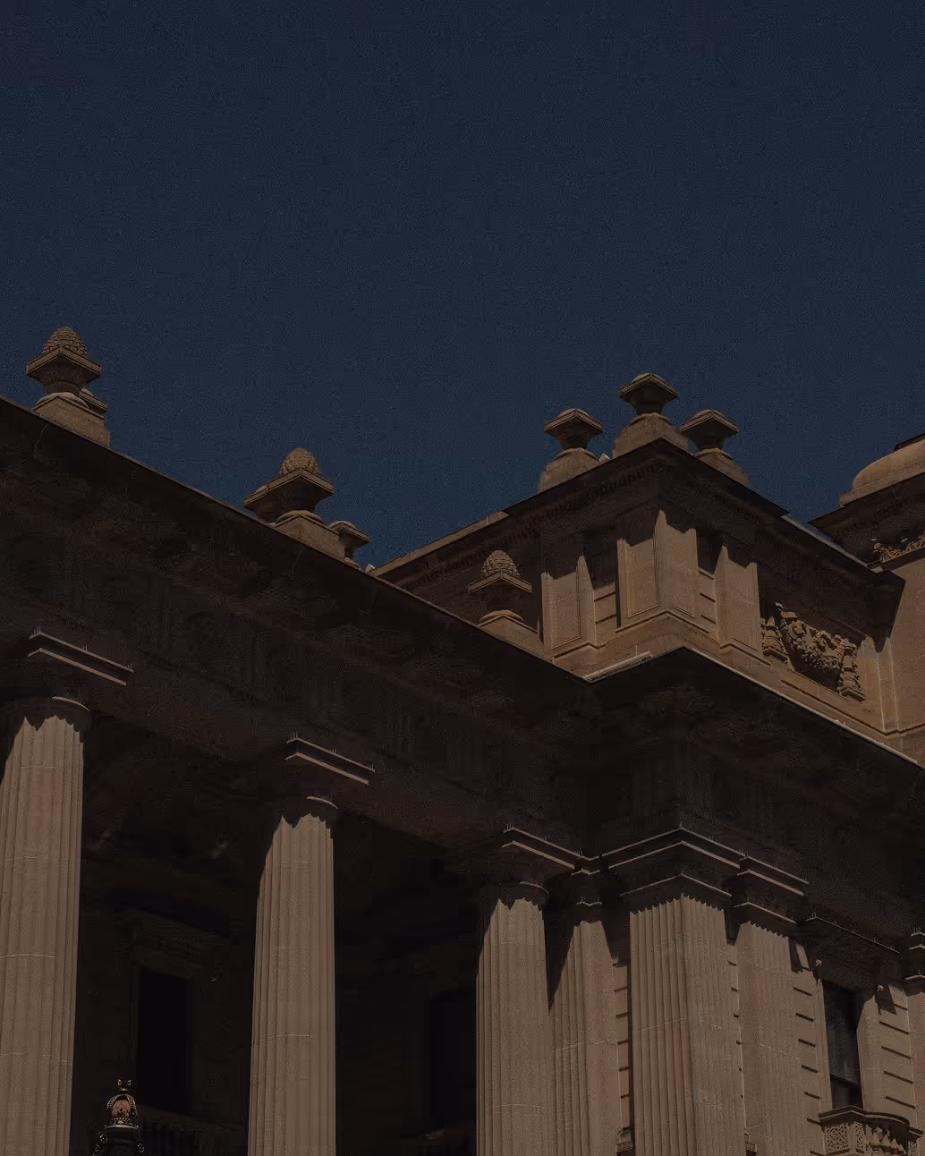 Ornate classical building facade with fluted columns and decorative architectural details under a clear night sky.