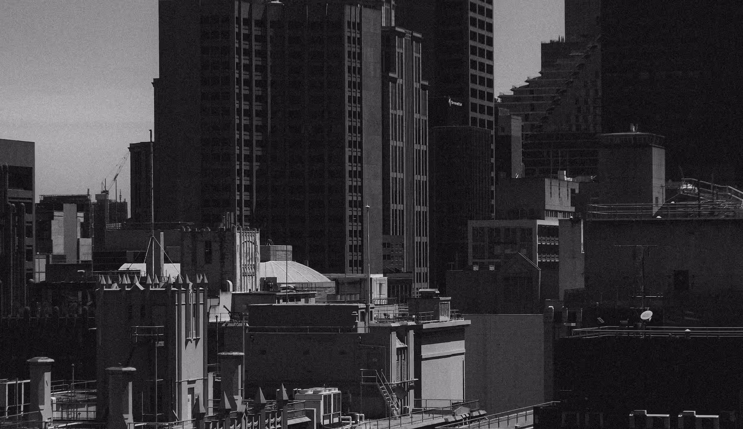 Black and white photo of city buildings with various rooftops, staircases, and antennas under daylight.