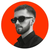 Portrait of a man with short hair and beard wearing black sunglasses and a black shirt, against an orange circular background.