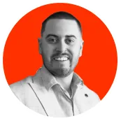 Portrait of a man with short hair and beard, smiling, wearing a light-colored suit jacket and white shirt, with an orange circular background.