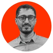 Portrait of a man with glasses, a trimmed beard, and short hair wearing a collared shirt in front of an orange circular background.