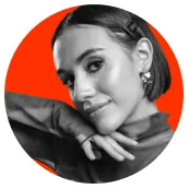 Black and white portrait of a young woman with short hair, resting her chin on her crossed hands against an orange circular background.