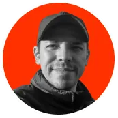 Black and white headshot of a man wearing a cap and jacket against a bright orange circular background.