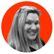 Smiling woman with long hair and glasses resting on her head, on an orange circular background.