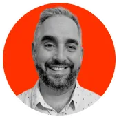 Smiling man with short gray hair and beard wearing a white shirt with a subtle pattern, against an orange circular background.
